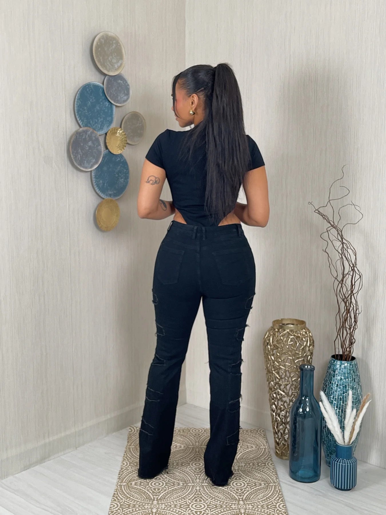 Woman in a black outfit standing in a room with decorative vases and wall art.