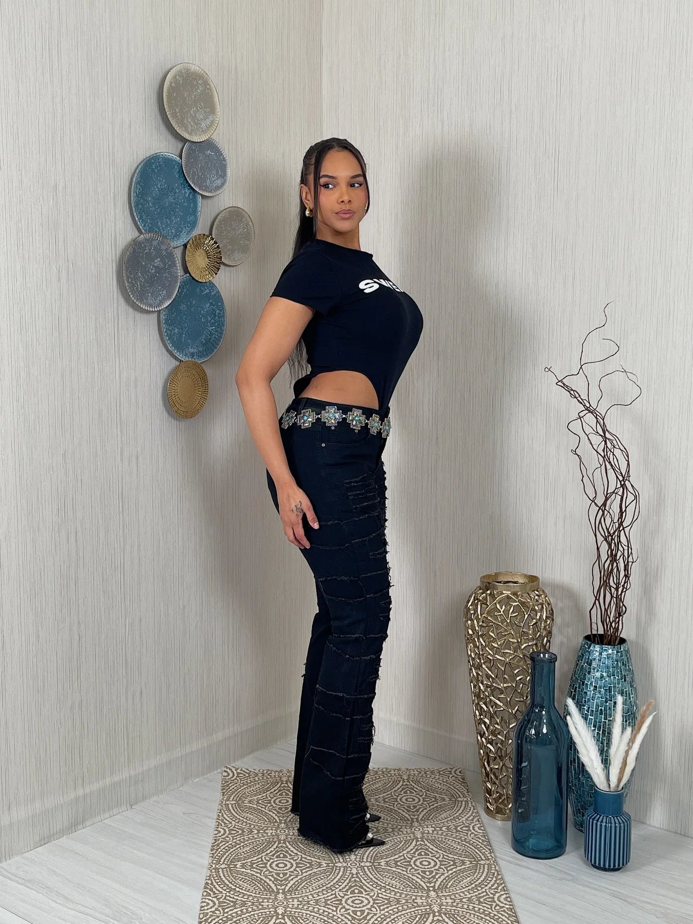 woman in a black outfit standing in a room with decorative vases and wall art.