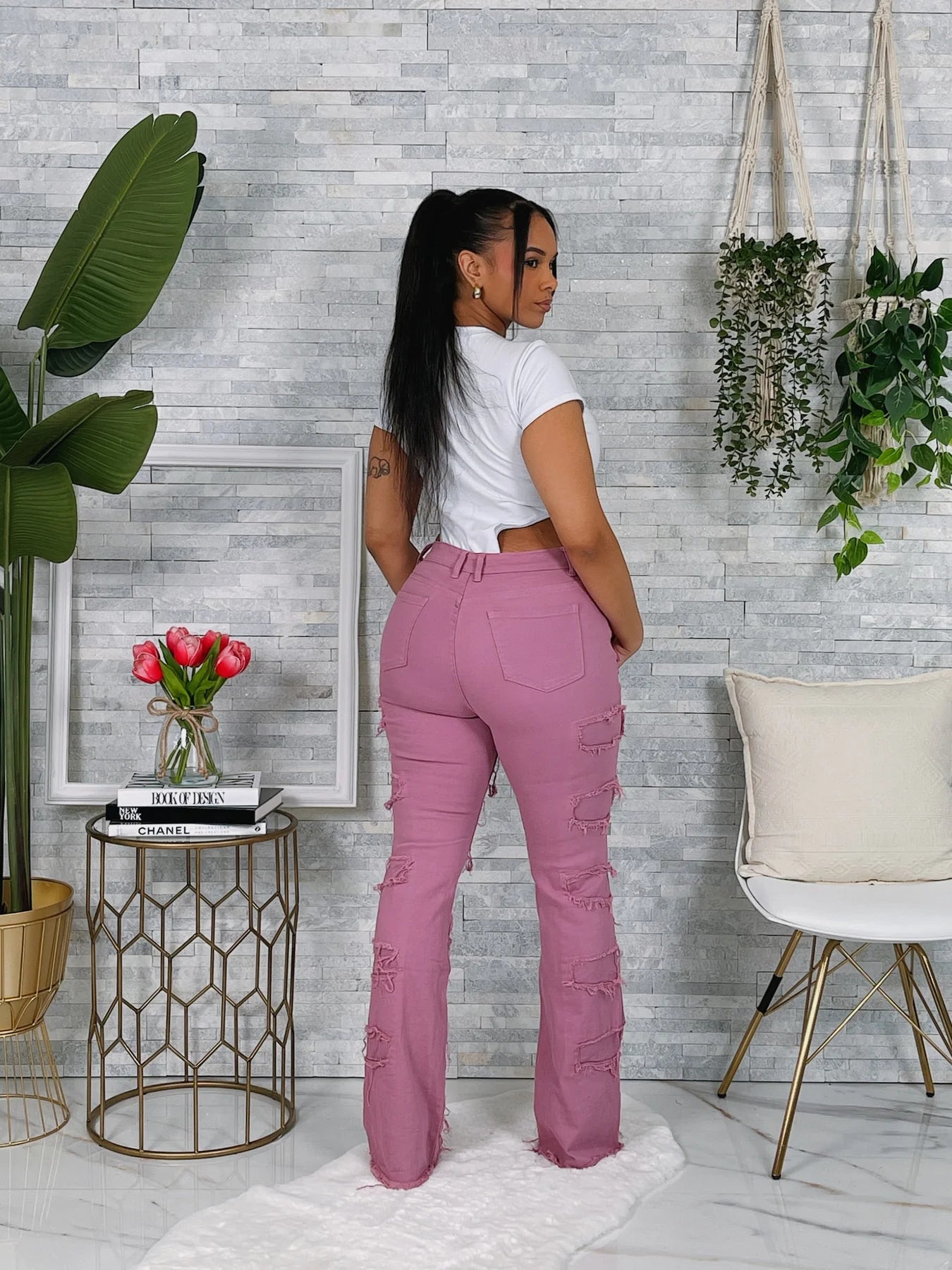 Woman wearing pink pants and a white top in a room with plants and a small table.