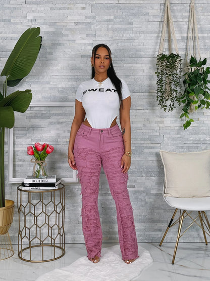 Woman wearing a white t-shirt with text and pink pants standing in a room with plants and decor.