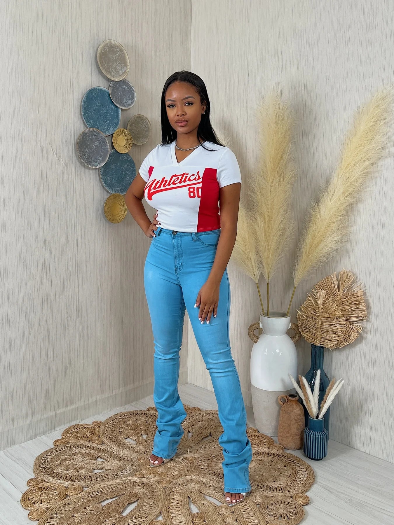 Woman wearing a white t-shirt with red accents and blue jeans standing in a room with decorative elements.