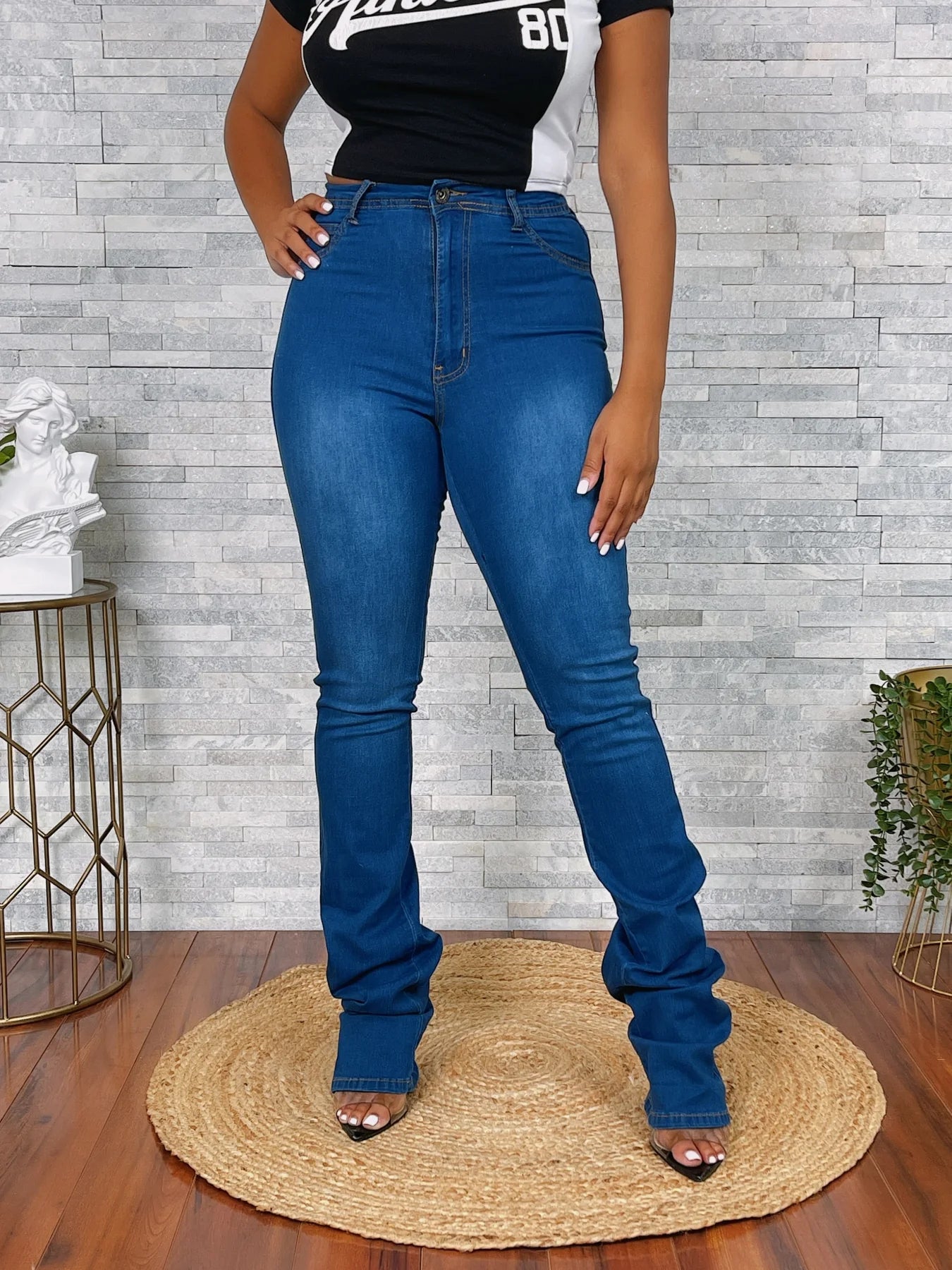 Person wearing blue jeans standing on a wooden floor with a gray brick wall background