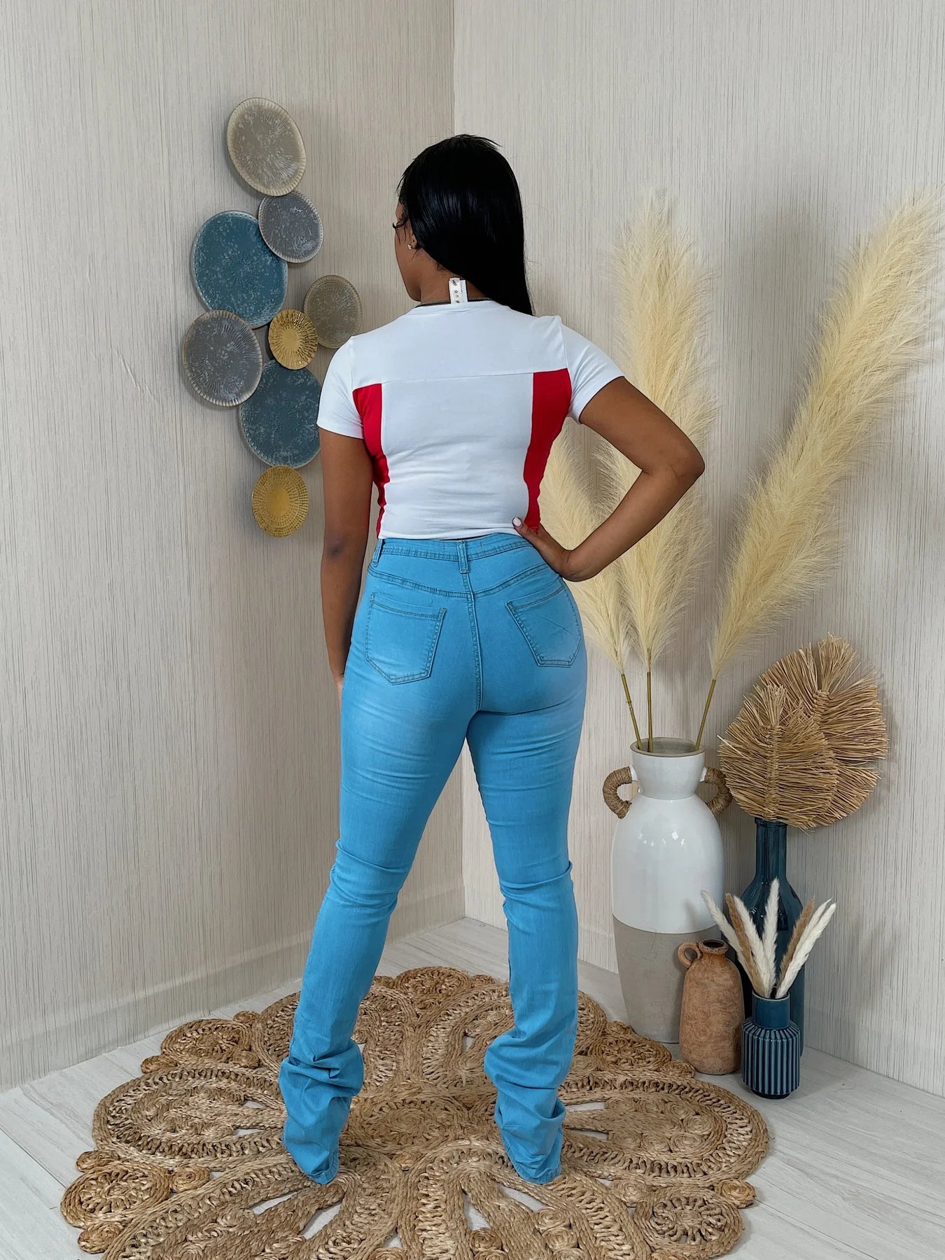 person wearing a white and red top with blue jeans standing in a room with decorative elements.