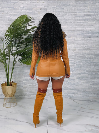 Person wearing a mustard yellow outfit with matching boots in a room with a plant and tiled floor.